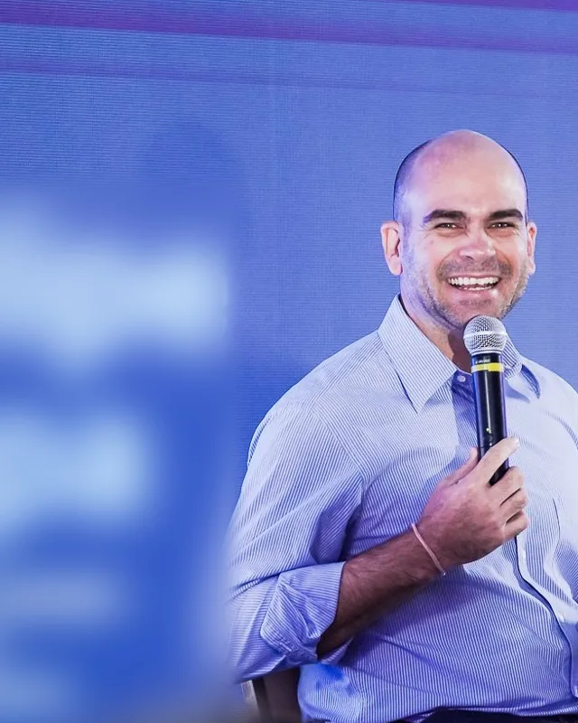 Felipe Lapa sentado no palco, ao microfone, sorrindo