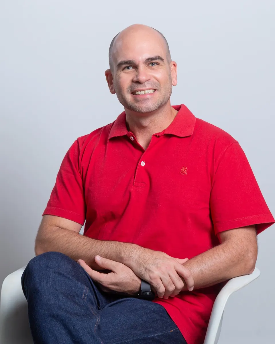 Felipe Lapa sentado, de camisa vermelha, sorrindo