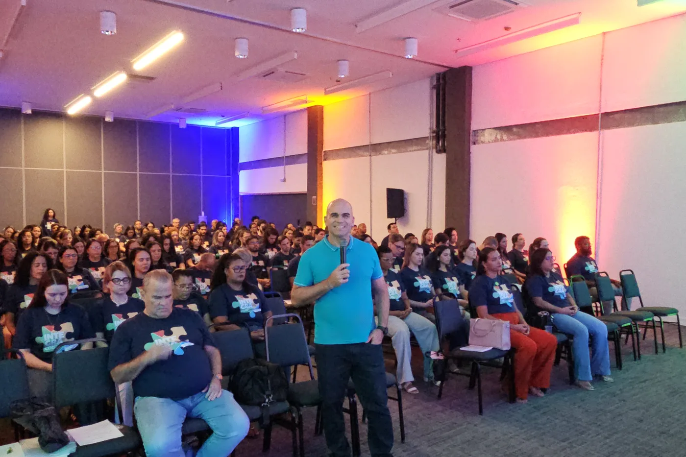 Felipe Lapa ao microfone, no meio de um auditório de educadores