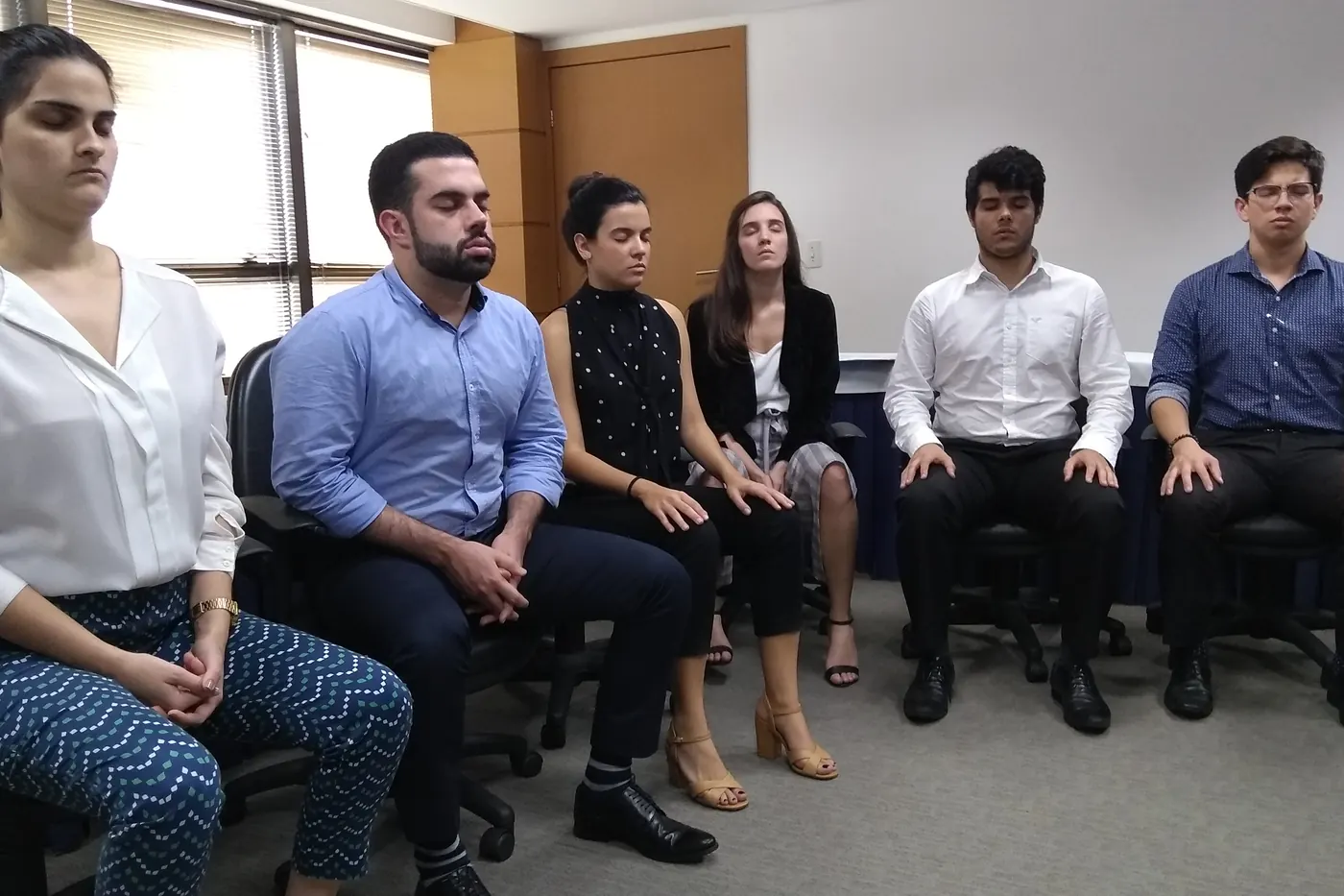 Equipe sentada em cadeiras, de olhos fechados, durante a prática num workshop